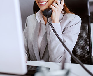 Gorgeous Caucasian businesswoman with long brown hair and in formal wear using computer and talking on the phone. Multitasking concept.